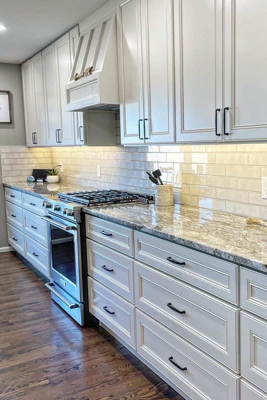 Off White Traditional raised kitchen cabinets with matt black pulls and marble countertops, 