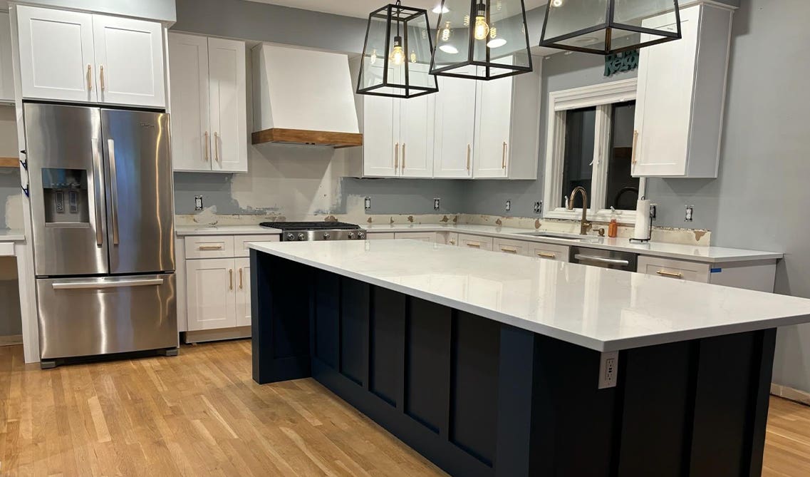 Two toned white and navy blue kitchen cabinets paired with bronze hardware and stainless steel appliances 