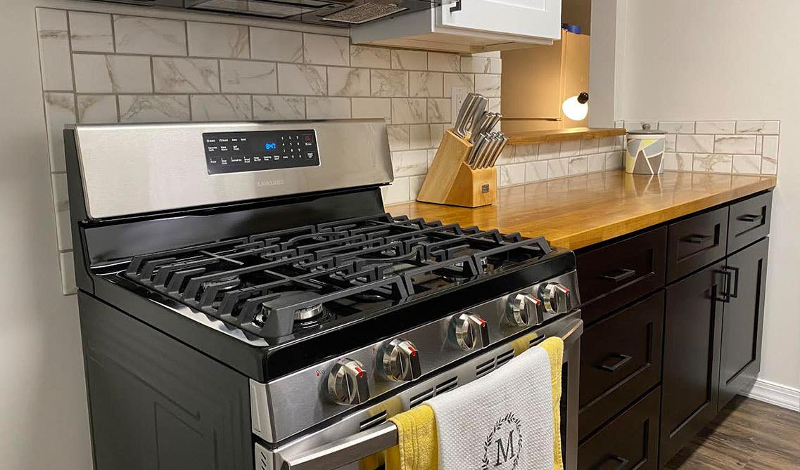 Brown and white two toned kitchen cabinets with wooden countertop, stove and microvan 