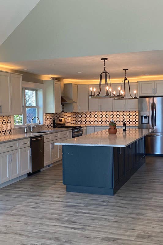 two toned kitchen feature linen and navy blue cabinets with ceiling lights and stainless steel hardware