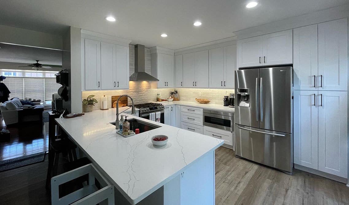 U-Shape Kitchen with white cabinets featured with white countertop, farmhouse sink, range hood, 