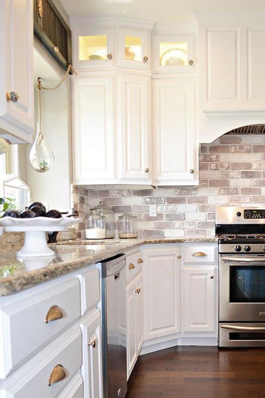 Red Brick Backsplash with white wall cabinets and brown countertop