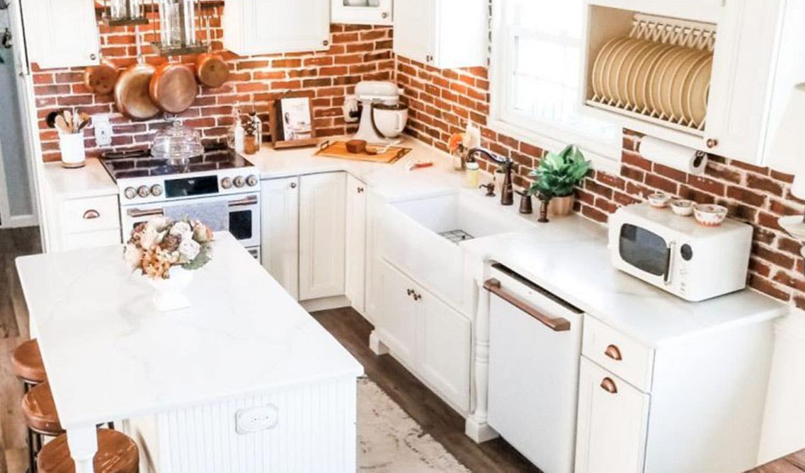 rustic kitchen design with white cabinets, metal hardware, small island, small window over sink, brick style backsplash 