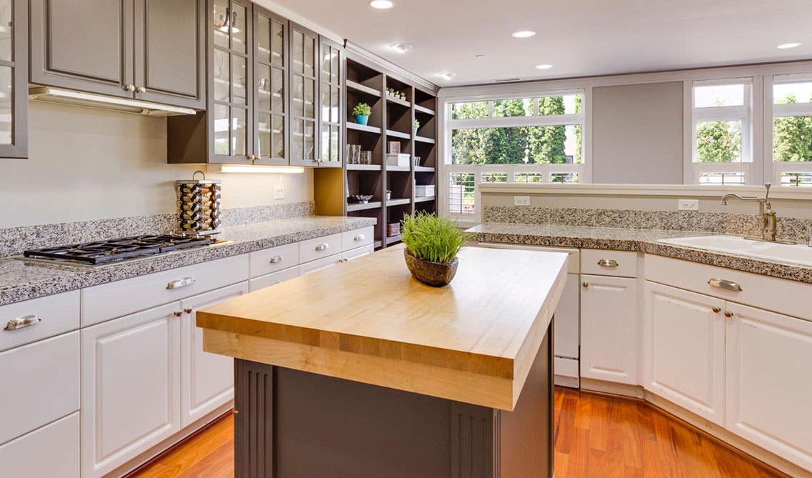 Farmhouse kitchen features White Base Cabinets With a Grey Island and wood countertops