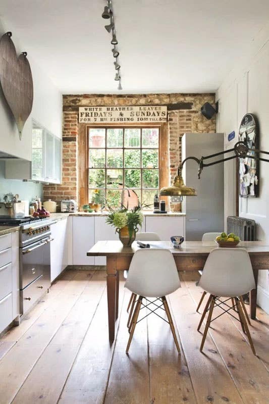 industrial rustic farmhouse kitchen with exposed brick wall, simple white cabinets, vintage wood table, simple white chairs and wood flooring
