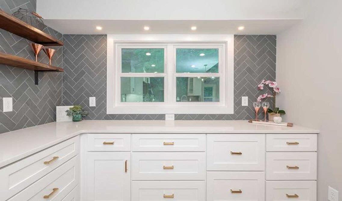 L shape kitchen with White shaker cabinets with gold handles, white countertop, open shelving, and pattern tile backsplash 