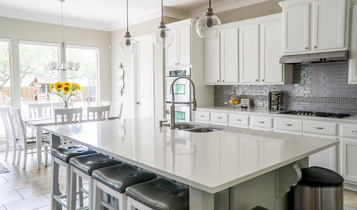 White Kitchen Design with large island, undermount sink, with stool chairs, pendent lighting, 