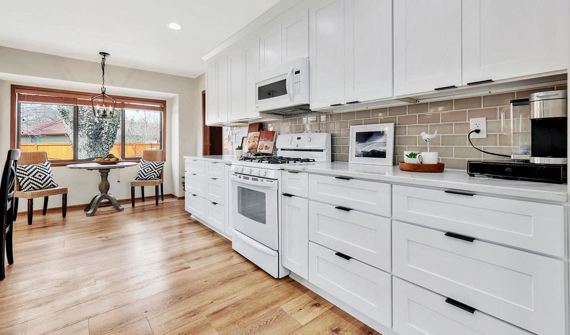 Single wall kitchen with white cabinets, tile backsplash, spc flooring and large window