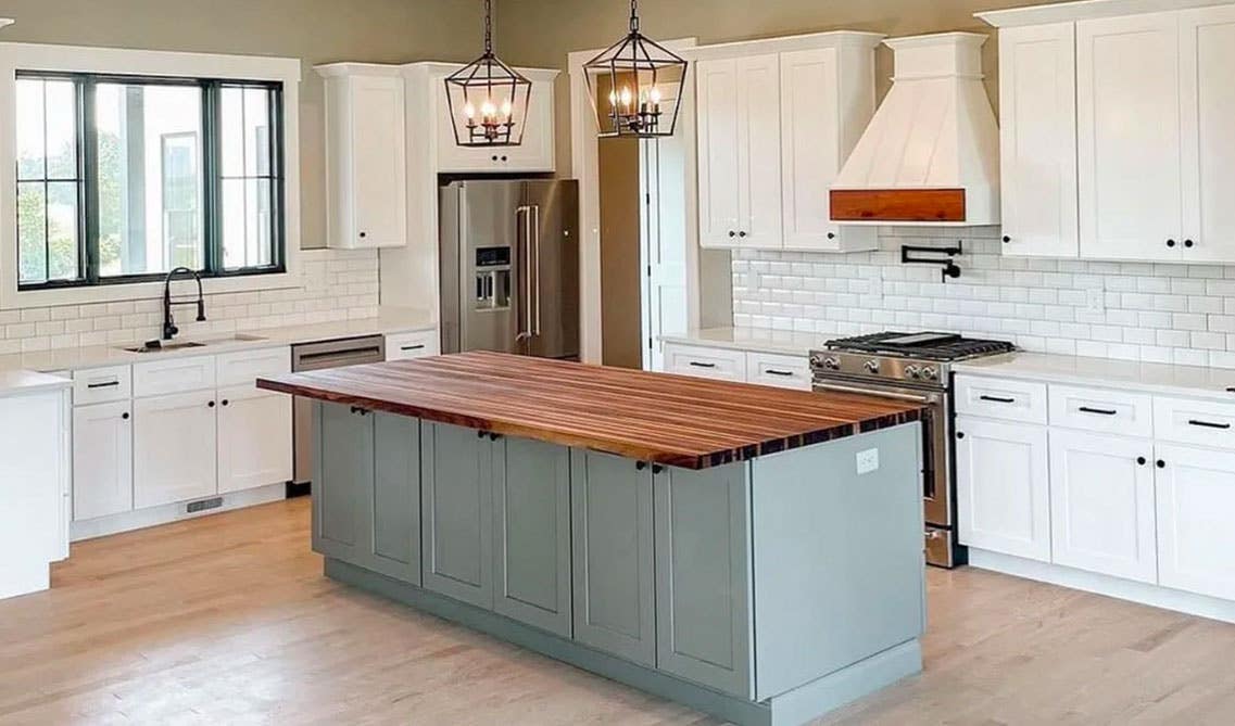 simple kitchen with white cabinets, black hardware, grey cabinet island, wooden countertop, wood range hood, pendent lights, spc flooring