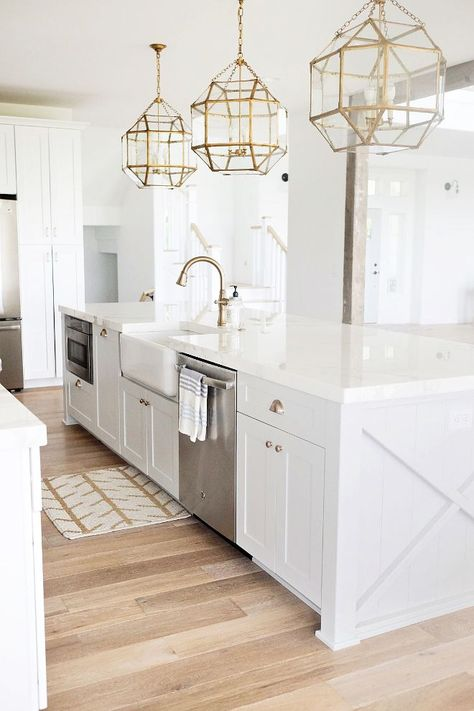 all white kitchen with gold geometric pendant lighting, light wood floors and oversized center island with farmhouse sink