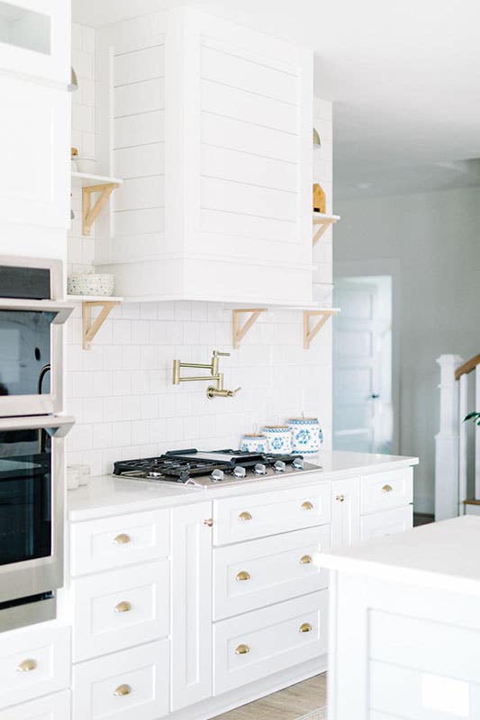 white kitchen with shaker cabinets and ducted range hood and gold hardware 