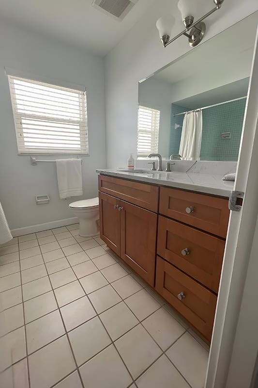 Natural wood bathroom vanity paired with marble countertop, large mirror and tile flooring 