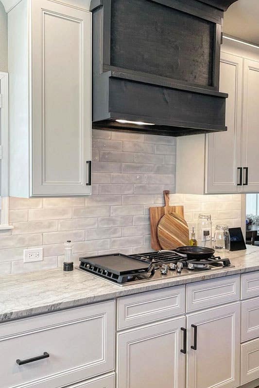 Kitchen design with white shaker cabinets, black pulls and black wood hood