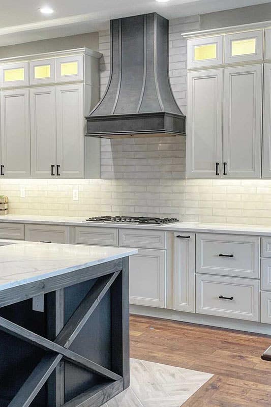 Rustic kitchen with white shaker cabinets, subway tile backsplash, wood hood, and wood flooring