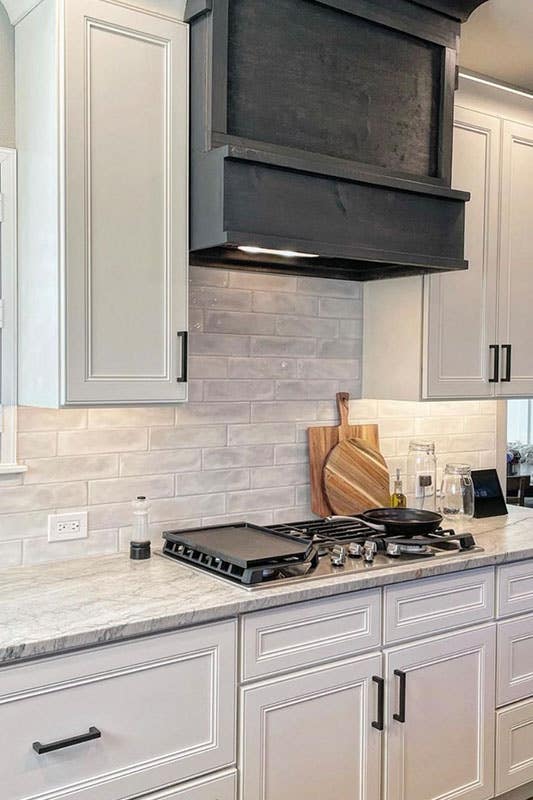 linen cabinets featured with black hardware, subway tile, black hood, and marble countertop 