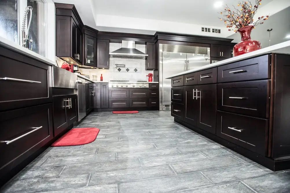 Brown Kitchen Cabinets with silver pulls and knobs, stainless steel appliances, and tile flooring 