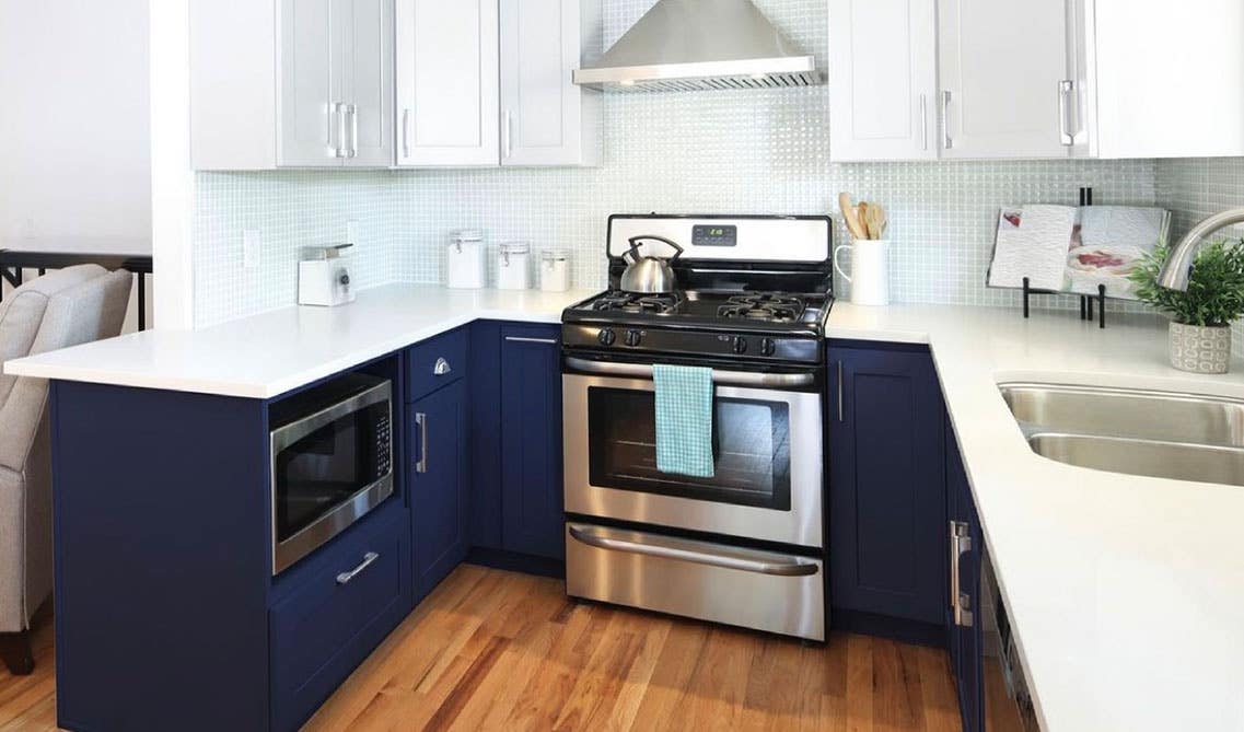 Small dual tone kitchen with shaker cabinets, white marble countertop and wooden flooring, stainless steel appliances