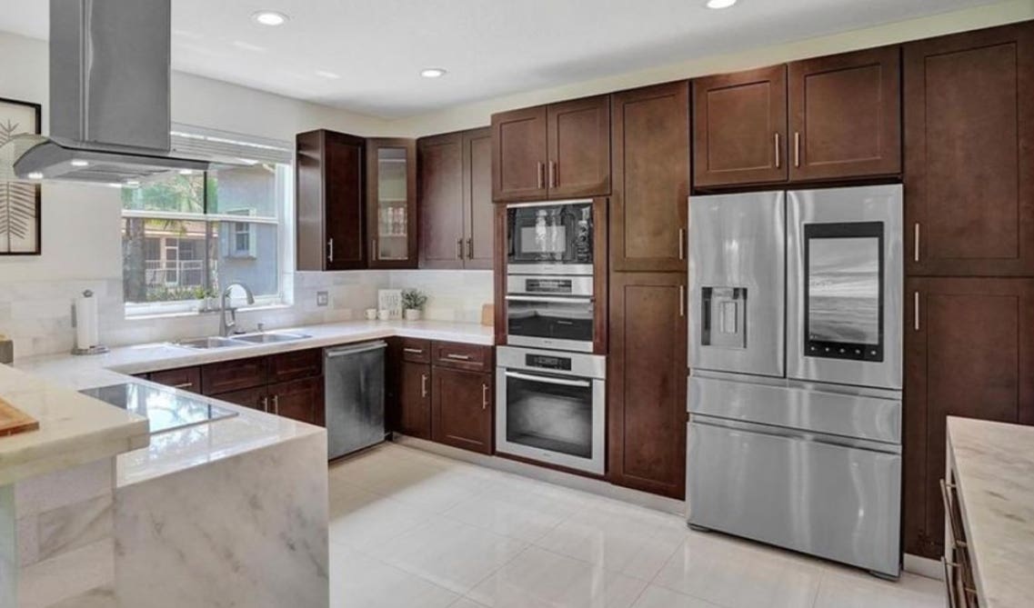 Brown kitchen cabinets paired with stainless steel appliances, waterfall countertop, and farmhouse sink 