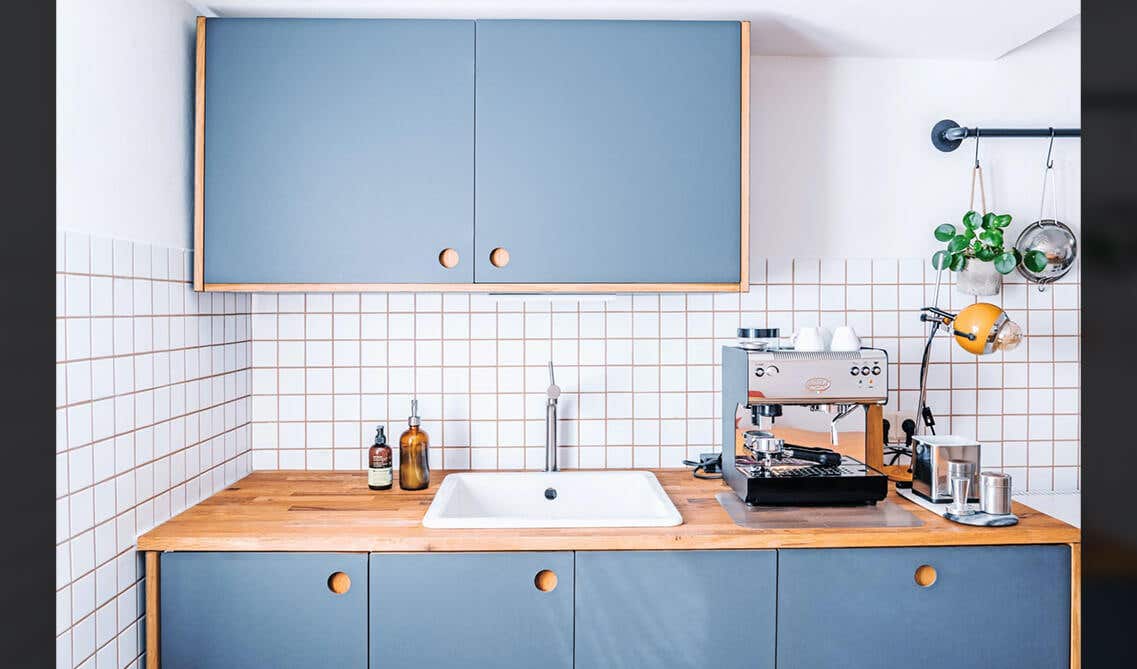 Vintage kitchen with blue cabinets set against a stark white background with sink and coffee machine