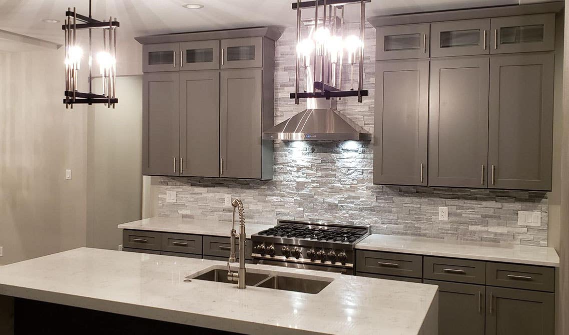 One wall kitchen with gray cabinets, tile backsplash, large countertop with undermount sink and stainless steel appliances