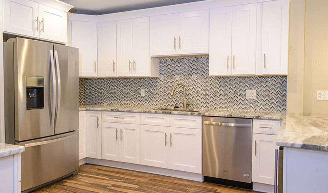 Kitchen with White Shaker cabinets with pattern backsplash wallpaper and stainless steel appliances 