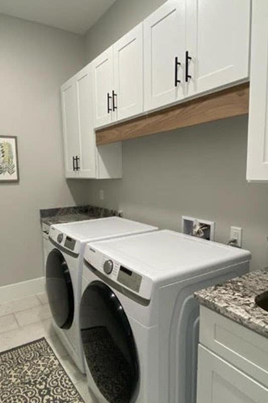 Small Laundry Room with washer and dryer, upper white cabinets, tile flooring, 2 wall art, 