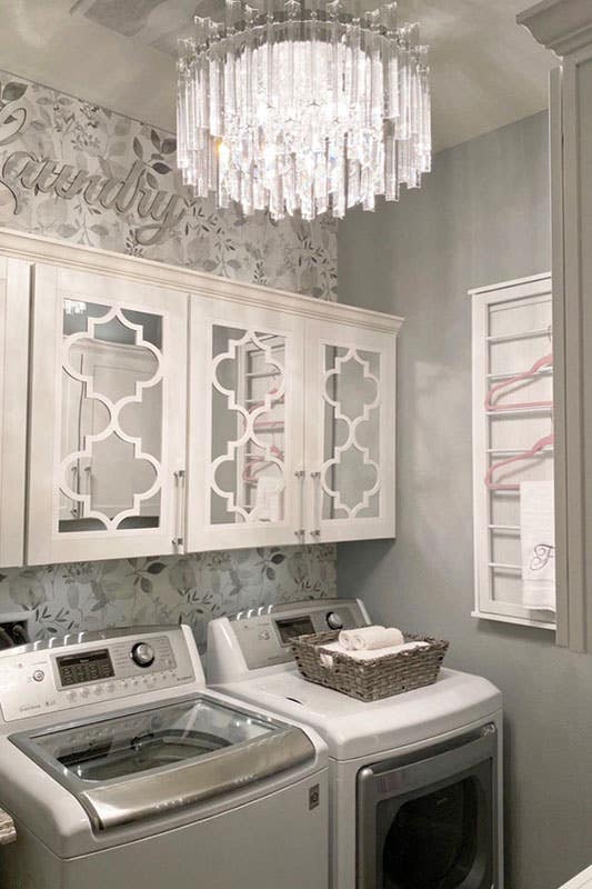 Stylish laundry with big chandelier and cabinet with glass door