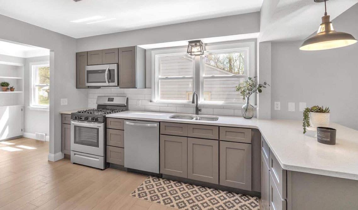 A kitchen with gray cabinets, white marble countertops with double bowl sink, and stainless steel appliances