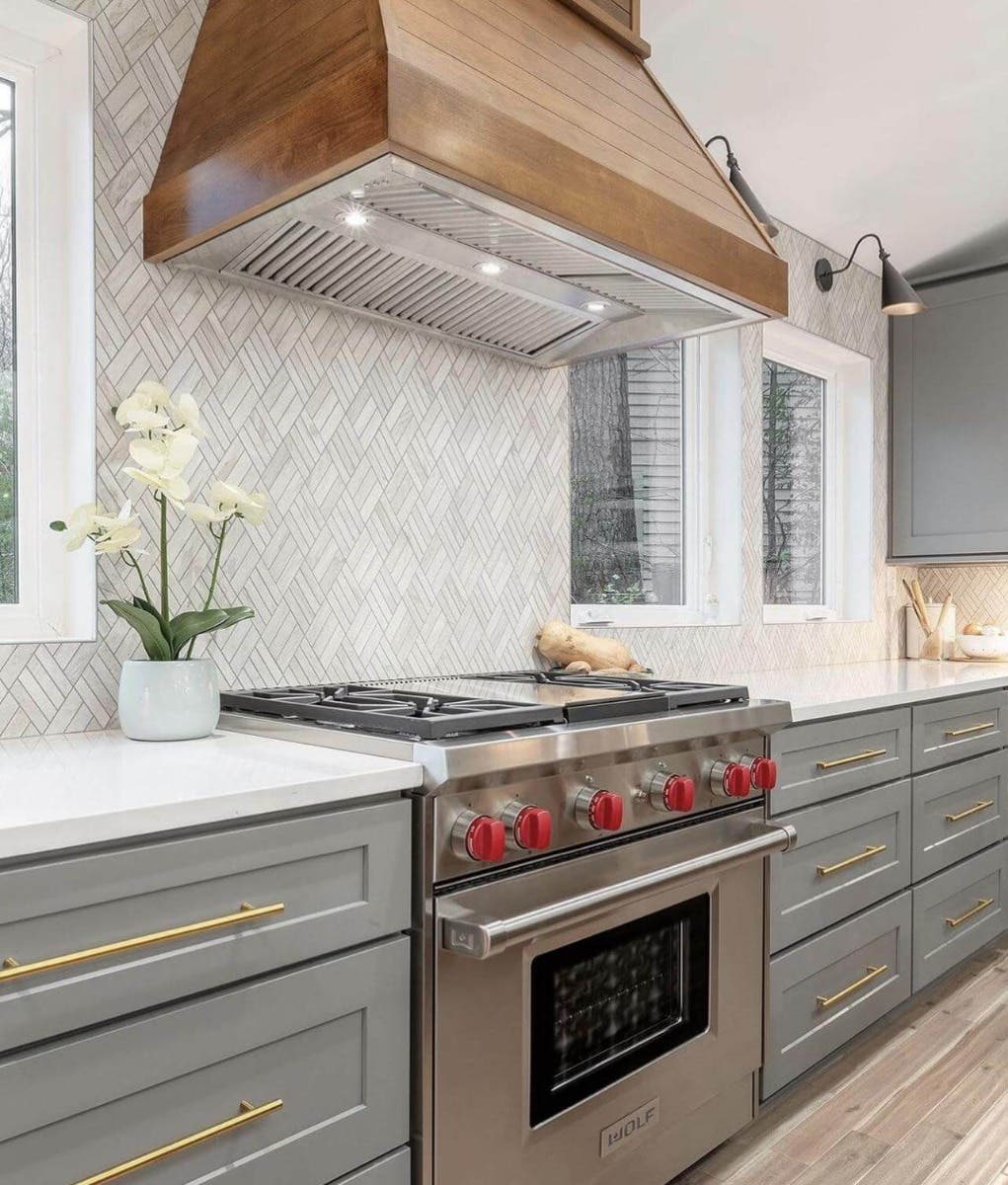 Kitchen with gray cabinet, gold decorative hardware, white countertop, pattern backsplash, and wood hood