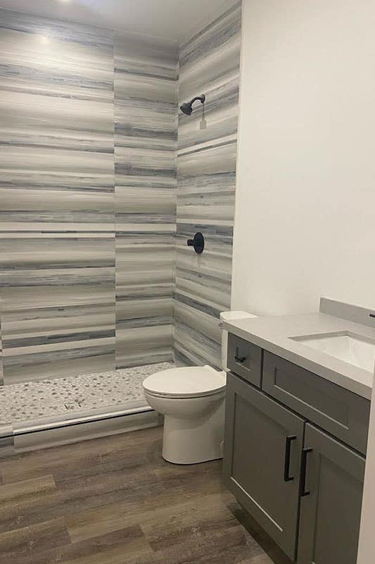 Simple bathroom with grey vanity and black fixture, tile flooring and, separate bathroom area