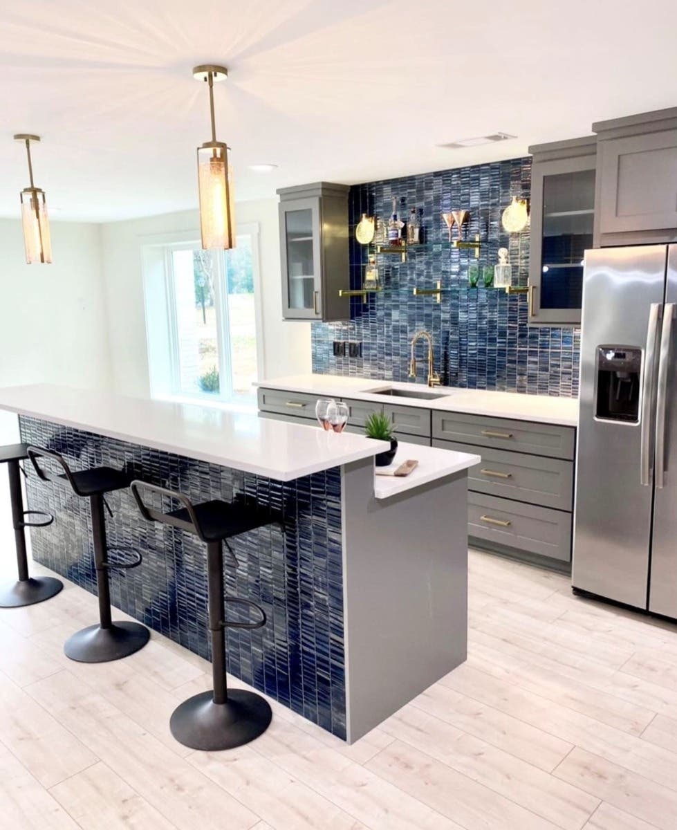 Split height island in L shape kitchen with gray cabinets and blue subway tiles