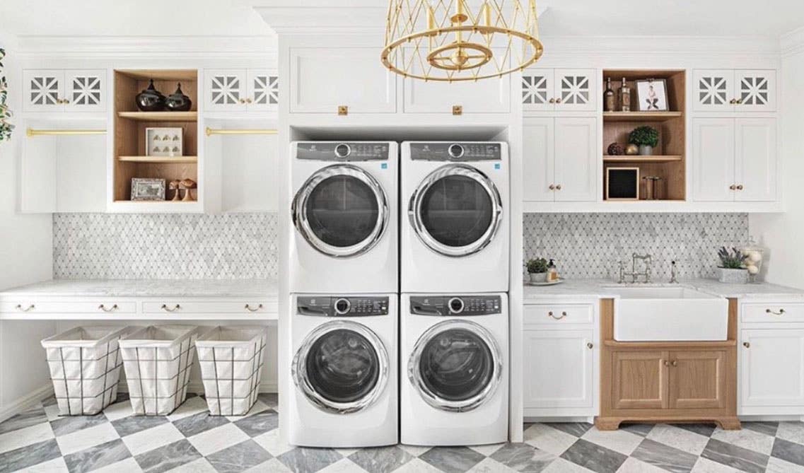 Modern laundry room with white storage cabinets, gold accents, washer and dryer, and baskets