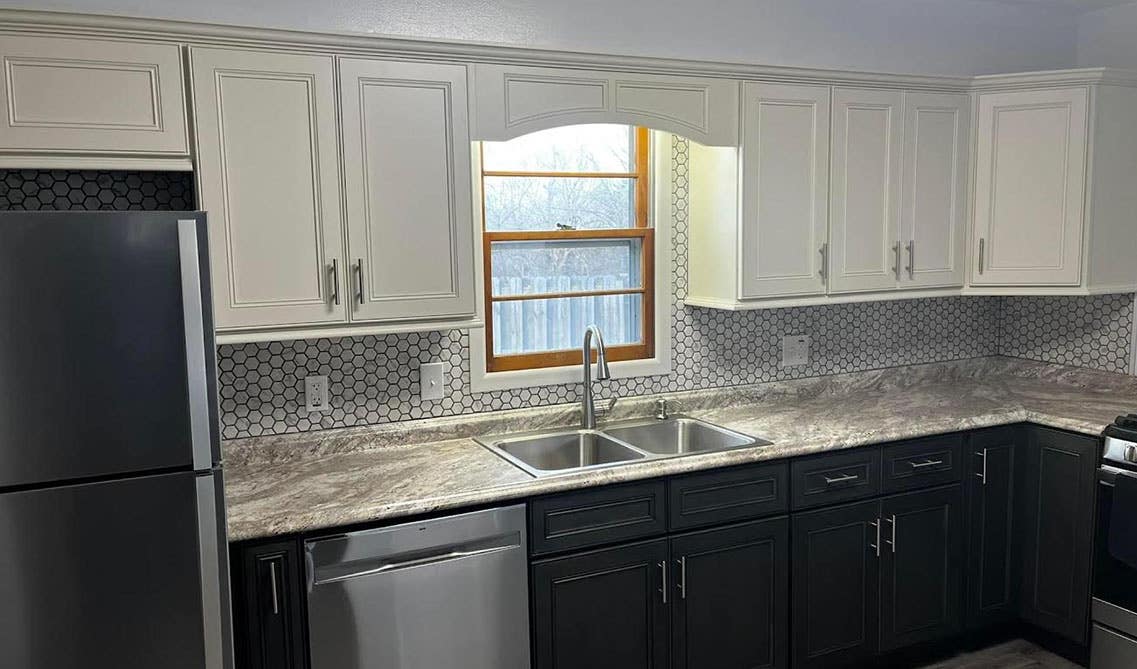 Kitchen with two tone white and black cabinets, marble countertop, and stainless steel appliances