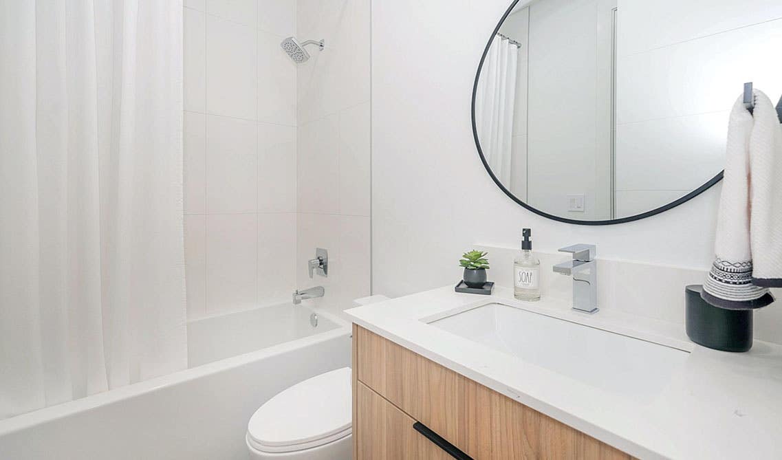 Modern bathroom design with natural wood vanity with sink, oval shape mirror and separate shower area