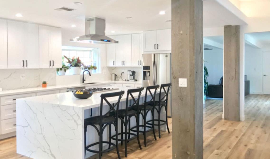 White kitchen design with shaker cabinets and large island with waterfall countertop, black themed chairs