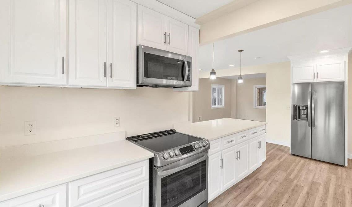 Small minimalist kitchen with shaker cabinets, white marble countertop wooden flooring, and stainless steel appliances