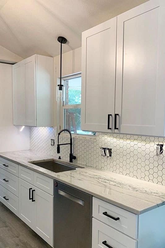 Kitchen design with white shaker cabinets, matt black pulls, stainless steel sink and marble countertop