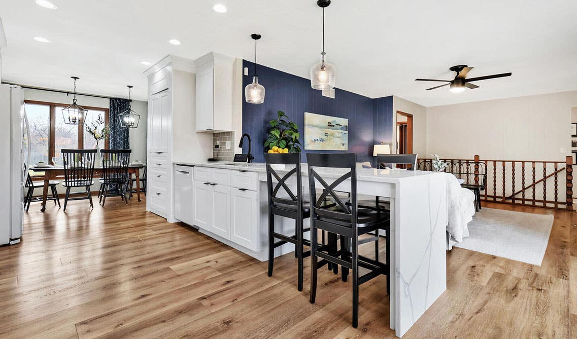 Stylish kitchen design, white shaker cabinets with extended island and marble waterfall countertop, navy blue accent wall 